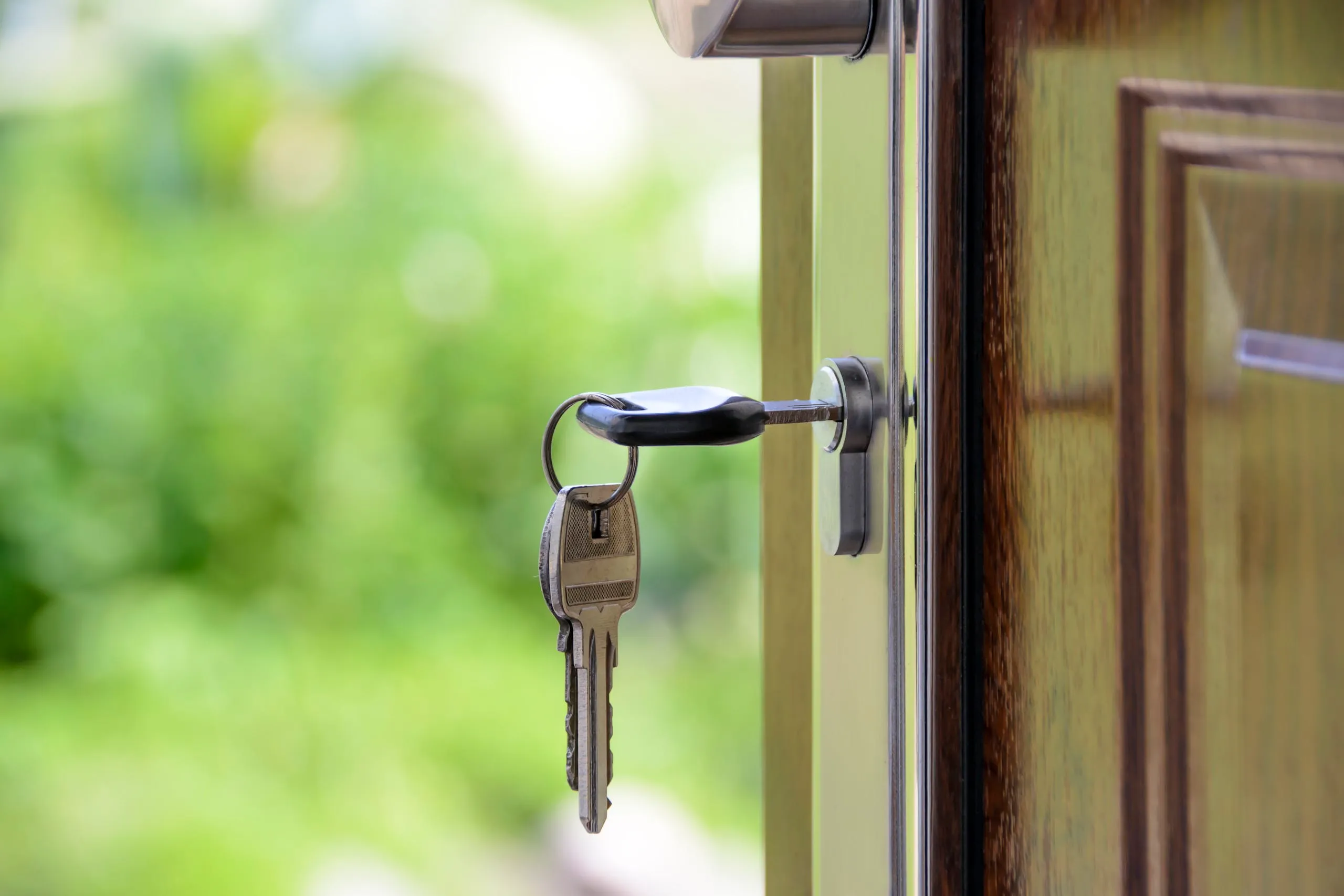 Clés suspendues à la poignée d'une porte en bois, symbole d'accès à une propriété. L'arrière-plan verdoyant suggère un cadre naturel paisible, idéal pour une maison à vendre dans la région de l'Outaouais.