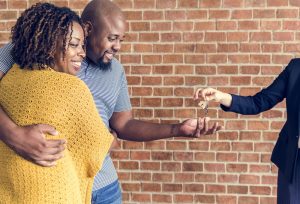 Couple rayonnant de joie, recevant les clés de leur nouvelle propriété des mains d'un courtier immobilier Gatineau. Valorisation immobilière réussie et vente maison par agent immobilier Outaouais qualifié.
